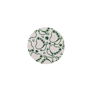 May include: A round, off-white coaster featuring a repeating pattern of green stethoscopes and shamrocks. The stethoscopes are stylized into heart shapes, with shamrocks adorning the curves. The design is a festive nod to St. Patrick's Day.