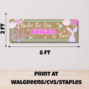 May include: A rectangular banner measuring 0.6 metres by 1.8 metres with a tan background, featuring the text Under the Sea ABIGAIL is Three! in pink and white. The design includes illustrations of pink starfish, seashells, coral, and bubbles.