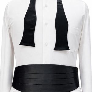 May include: A formal outfit comprising a white dress shirt, a black bow tie, and a cummerbund. The bow tie is pre-tied and hangs down the shirt front. The cummerbund is pleated and encircles the waist.