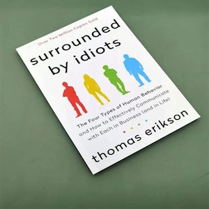 May include: A white book titled Surrounded by Idiots by Thomas Erikson. The cover features four human silhouettes in red, yellow, green, and blue, with the text Over Two Million Copies Sold and The Four Types of Human Behavior.