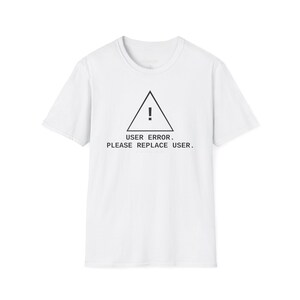 Op de afbeelding: Wit T-shirt met een zwart driehoekig waarschuwingssymbool en de tekst "USER ERROR. PLEASE REPLACE USER." eronder. Het shirt heeft korte mouwen en een ronde hals.