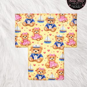 May include: Yellow fleece blanket with a repeating pattern of teddy bears in sailor outfits and pink dresses, sailboats, and red hearts. The blanket has a rounded shape and the text "Fancy Fleece Connection" is at the bottom.