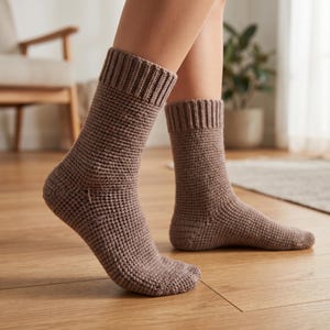 Può includere: Un paio di calzini marroni a maglia con polsini a coste. I calzini hanno un aspetto strutturato e tessuto e sono indossati sui piedi di una persona. I calzini sono di colore neutro e sembrano fatti a mano.