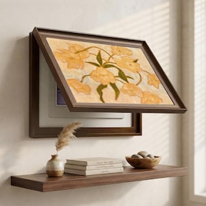 Puede incluir: Un marco rectangular de pared en color marrón oscuro con un panel frontal abatible que muestra una pintura de flores amarillas con hojas verdes. Debajo del marco hay un estante de madera con un jarrón de cerámica y tres libros.