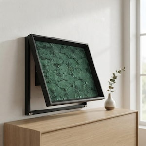 Puede incluir: Un televisor rectangular montado en la pared con un marco negro fino que muestra un patrón abstracto texturizado en verde oscuro. La pantalla está inclinada hacia afuera desde la parte superior, revelando un soporte negro.