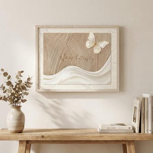 May include: Framed artwork with a beige textured backdrop, a white butterfly, and a flowing white fabric design. The cursive text reads "New butterfly". The frame is made of light-coloured wood.