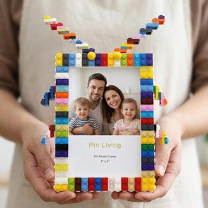 Könnte beinhalten: Ein rechteckiger Bilderrahmen aus bunten Kunststoff-Bausteinen. Der Rahmen verfügt über zwei antennenartige Strukturen an der Oberseite und zeigt ein Familienfoto mit dem Text Pin Living DIY Photo Frame 4" x 6".
