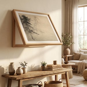 May include: A framed artwork featuring a monochrome landscape scene of trees, mounted on a light-colored wall. The artwork is in a light wood frame, and the scene is rendered in shades of gray and beige. The room has a rustic, natural aesthetic.