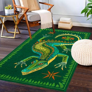 Könnte beinhalten: Ein rechteckiger Teppich mit einer großen, detaillierten Illustration eines grünen und gelben Alligators auf dunkelgrünem Grund. Das Design enthält orangefarbene sternartige Akzente und eine dekorative Bordüre aus kleinen blattartigen Formen.