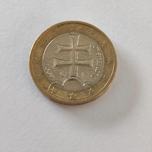 Puede incluir: Una moneda de un euro con un anillo exterior dorado y un centro plateado. La moneda presenta un diseño de doble cruz y el año 2009. La palabra "SLOVENSKO" está inscrita alrededor del borde.