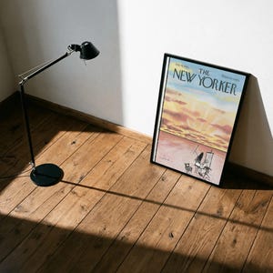 May include: A framed magazine cover of The New Yorker dated July 16, 1983, featuring a watercolor illustration of a sunset over a desert landscape with an artist painting at an easel, displayed in a black frame next to a black metal desk lamp.