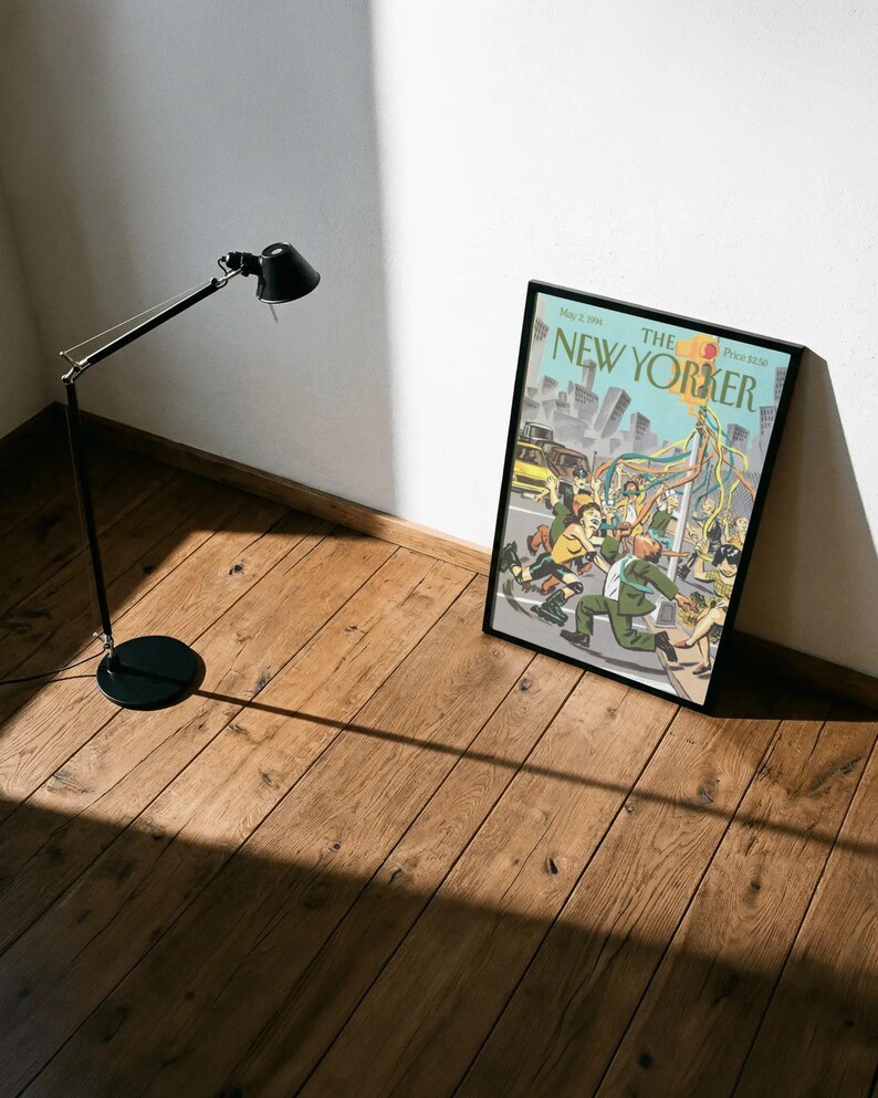 May include: A framed magazine cover titled The New Yorker dated May 2, 1994, featuring a colorful illustration of people dancing around a maypole in a city street with skyscrapers in the background, enclosed in a simple black frame.