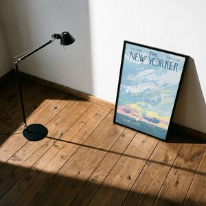 May include: A black adjustable floor lamp with a round base stands next to a framed New Yorker magazine cover. The magazine cover features a colorful sky scene with the text "The New Yorker". The items are on a wooden floor.