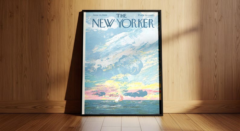 May include: Framed New Yorker magazine cover from June 14, 1982, featuring a seascape with a sailboat under a cloudy sky. The artwork is in shades of blue, pink, and yellow. The magazine is displayed on a wooden floor and leaning against a wooden wall.