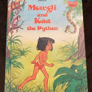 May include: A vintage Walt Disney Productions book titled Mowgli and Kaa the Python. The cover features a cartoon illustration of Mowgli walking through a jungle with monkeys in the trees and a large python snake hanging from a branch above.