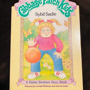 May include: A vintage "Cabbage Patch Kids" storybook titled "Sybil Sadie." The cover shows a girl in a pink top and blue jeans with a basketball. The book is a Parker Brothers Story Book.