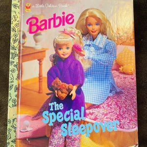 Op de afbeelding: Een kinderboek getiteld "Barbie The Special Sleepover" van Little Golden Book. De omslag toont twee Barbie-poppen, een in een paarse badjas met een teddybeer, de andere in een blauw geruite nachtjapon. De achtergrond is roze met bloemmotieven.