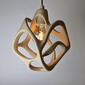 Puede incluir: Una lámpara colgante con una estructura beige orgánica similar a una celosía con una superficie texturizada. El marco geométrico rodea una bombilla de vidrio transparente con un filamento brillante visible, suspendida por un cable negro fino.