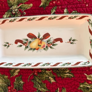 May include: A rectangular white ceramic serving tray featuring a central illustration of pears and peaches accented by green holly leaves and a red ribbon. The border is decorated with a repeating pattern of red ribbons and green holly leaves.