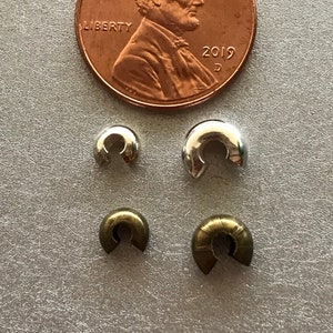 May include: Four crimp end bead tips, two silver and two gold, shown next to a US penny for size comparison.  The penny is dated 2019.