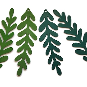 May include: Four green leaf-shaped metal cutouts in varying shades of green, arranged on a white background. Each cutout has a small hole at the top. The leaves have a simple, stylized design, perfect for crafting or decorative purposes.