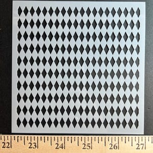 May include: A white plastic stencil with a repeating diamond pattern. The stencil is square and has a ruler along the bottom edge, measuring from 22 to 27 inches.