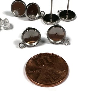 May include: A collection of silver-colored earring posts with round settings, earring backs, and a penny. The earring posts have a small loop for attaching charms. The penny is dated 2020.