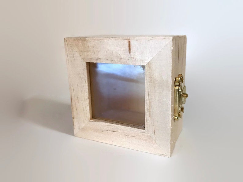 May include: A small, white wooden box with a glass front and a brass latch. The box has a distressed finish and is ideal for displaying small items.