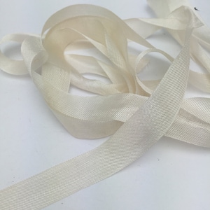 May include: A close-up of a spool of off-white satin ribbon. The ribbon is soft and silky, and it has a subtle sheen.