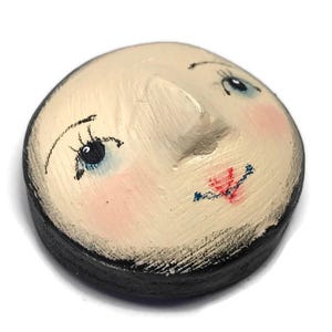 An angled view of the round plaster doll head showing its three-dimensional nose and dark-painted side rim.