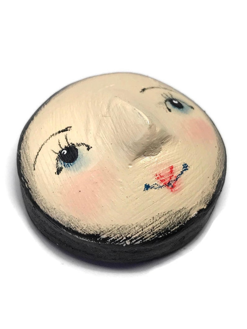 An angled view of the round plaster doll head showing its three-dimensional nose and dark-painted side rim.