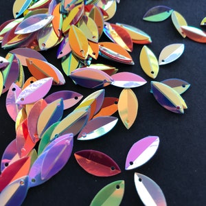 May include: Assortment of iridescent leaf-shaped sequins in various colors, including purple, pink, green, orange, and red. The sequins are scattered on a black background.