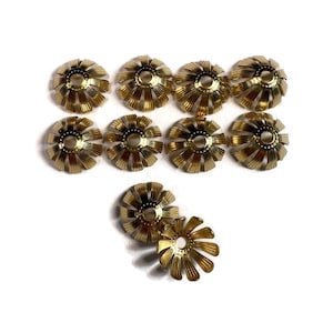 May include: A collection of ten gold-colored, flower-shaped bead caps. Each cap has a central hole and radiating petal-like structures. The caps are arranged on a white background, with two caps slightly separated from the others.