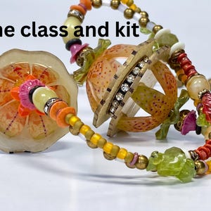 Pode incluir: Um colar com uma conta esférica laranja estampada com uma fila central de strass transparentes, acompanhada por uma conta plana circular com motivos florais laranja, enfiada com contas de vidro, metal e cristal. Texto: online class and kit.