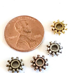 May include: Four small, circular metal beads with a spiky, sunburst-like texture arranged around a copper-colored 2016 United States penny. The beads are finished in gold, silver, bronze, and antique brass tones, each featuring a central hole.
