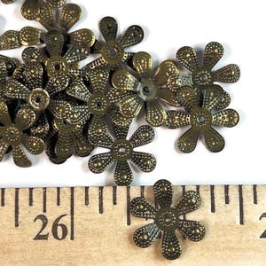 May include: A collection of antique brass-colored metal flower-shaped beads with six petals and a central hole. The beads feature a textured, dotted surface pattern. A wooden ruler is visible, showing one bead measures approximately 0.75 inches wide.