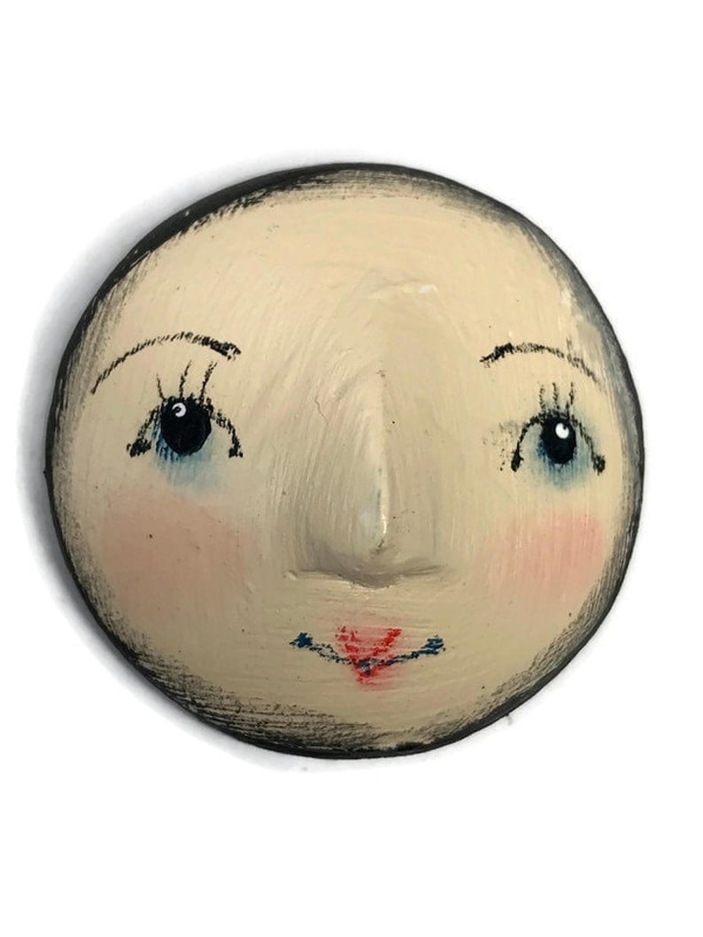 A flat-back round plaster doll head with hand-painted facial details including arching eyebrows, dark blue eyes, pink blush, and red lips.