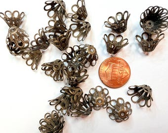 Può includere: Una collezione di coprinodo in metallo color bronzo antico con un design a petali in filigrana. Ogni coprinodo presenta un foro centrale e bordi smerlati. È inclusa una moneta da un centesimo degli Stati Uniti per mostrare la scala dimensionale.