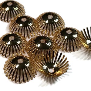 May include: A collection of gold-colored, decorative bead caps. Each cap has a fluted, petal-like design with a central hole. The caps are arranged on a white surface, showcasing their intricate details and metallic sheen. Ideal for jewelry making.