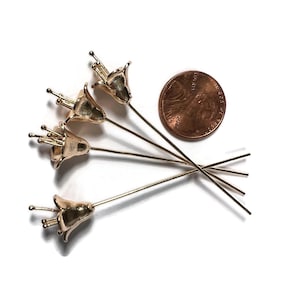May include: Five gold flower-shaped headpins with long, thin stems. The headpins are about the size of a US penny.