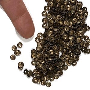 May include: A large pile of gold-colored metal flower-shaped embellishments. The embellishments have a small hole in the center.