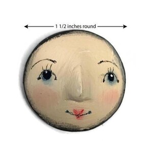 A close-up view of a hand-painted round plaster doll face with blue eyes, pink cheeks, and a dimension line indicating 1 1/2 inches round.