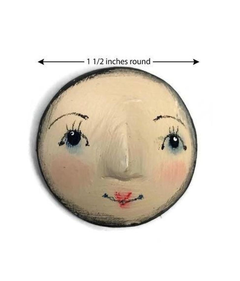 A close-up view of a hand-painted round plaster doll face with blue eyes, pink cheeks, and a dimension line indicating 1 1/2 inches round.