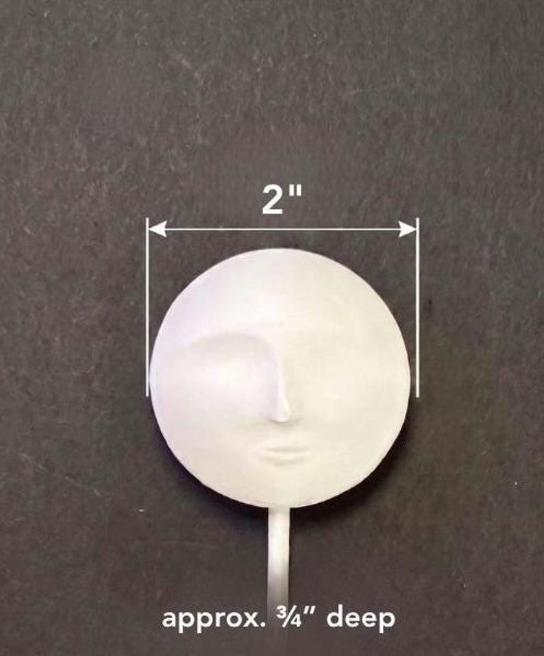 A white round plaster doll head on a stick with overlaid dimension arrows and text indicating two inches wide and approximately three-quarters of an inch deep.
