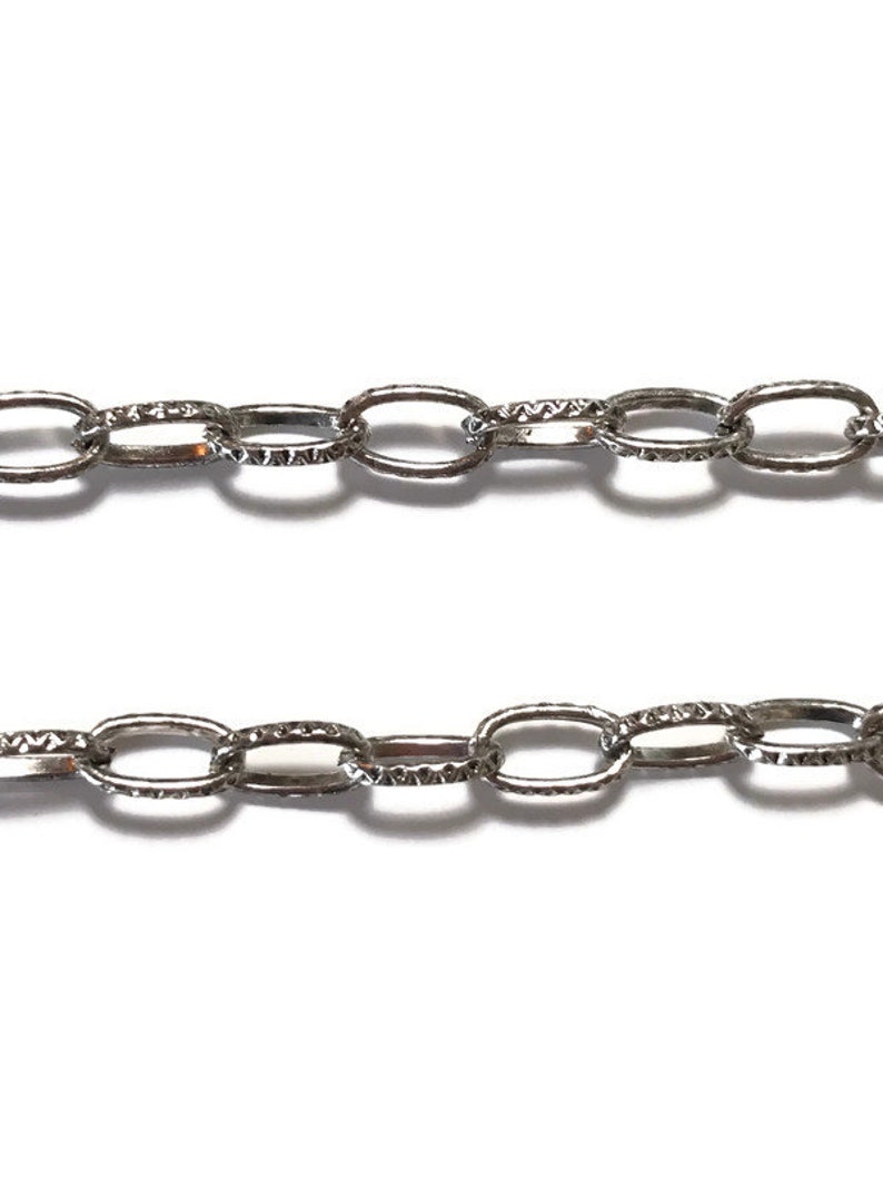 K&ouml;nnte beinhalten: Eine silberne Kette mit ovalen Gliedern. Die Glieder haben eine strukturierte Oberfl&auml;che.