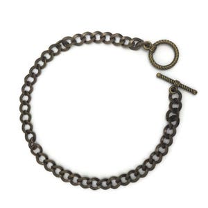 May include: A gold-toned chain bracelet with a toggle clasp. The chain is made of thick, linked metal.