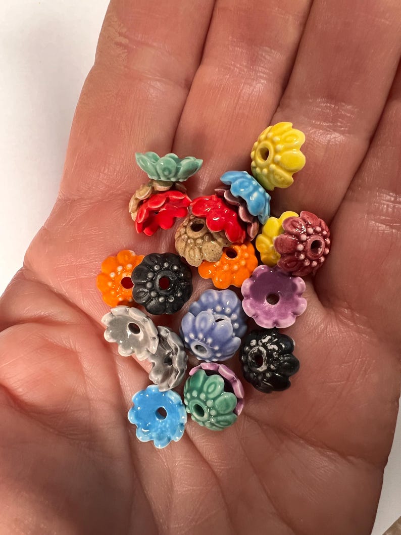 Pu&ograve; includere: Assortimento di perline di ceramica colorate a forma di fiore. Le perline hanno una variet&agrave; di colori, tra cui rosso, arancione, giallo, verde, blu, viola e nero. Le perline hanno un diametro di circa 2,5 cm.
