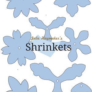 May include: A set of seven blue shrink plastic templates for crafting. The templates are shaped like flowers, leaves, and a star. The text "Julie Haymaker's Shrinkets" is printed in brown on the page.