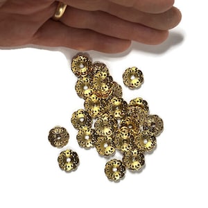 May include: A pile of gold-colored metal beads with a decorative floral design. The beads are round with a hole in the center.
