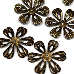 May include: Six antique gold metal flower embellishments with intricate cut-out designs. The flowers have a slightly raised center with a small hole in the middle.